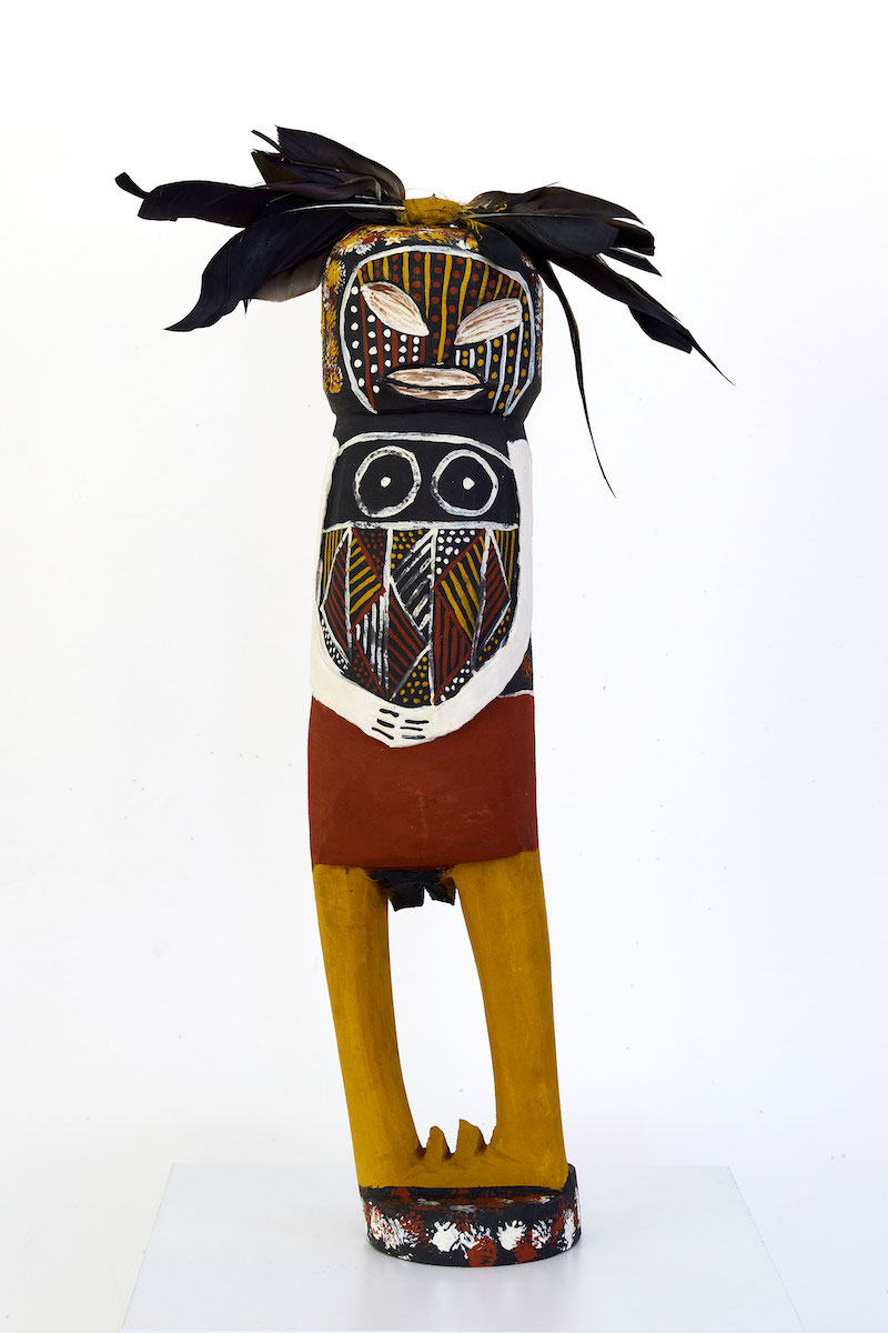 Carved figurative sculpture with head feathers and painted markings in black, red, yellow ochre and white.