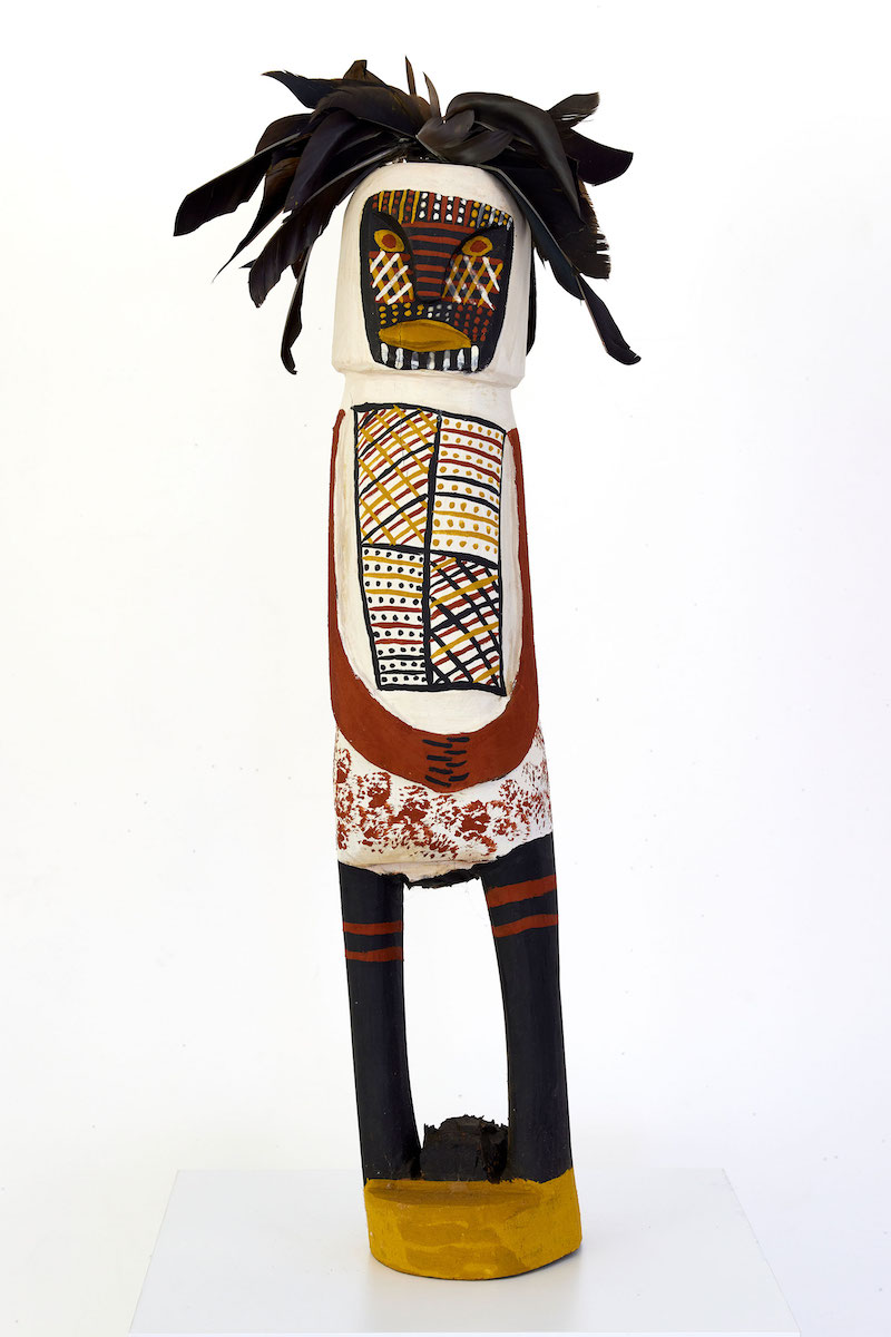 Carved figurative sculpture with head feathers and painted markings in black, red, yellow ochre and white.