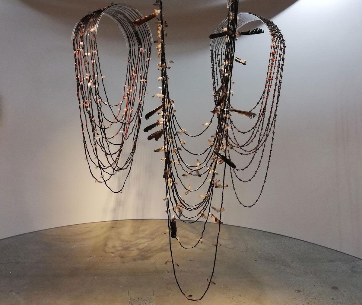 Three super-sized necklaces, made from river reeds and bird feathers, hanging from the ceiling
