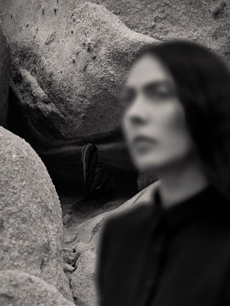 A black and white photograph of a blurred person wearing black against a background of boulders
