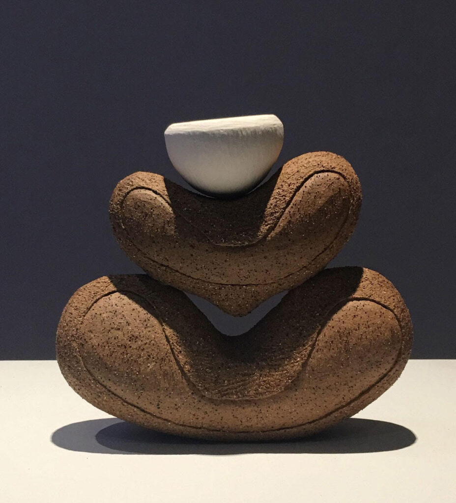 A large, abstract sculpture made of clay in brown and cream two-tone, with three segments getting smaller in size as it ascends.