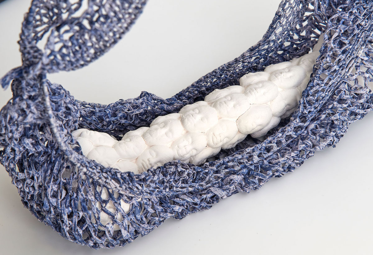 A piece of white ceramic carved into multiple faces, cradled within a woven blue-grey bag.