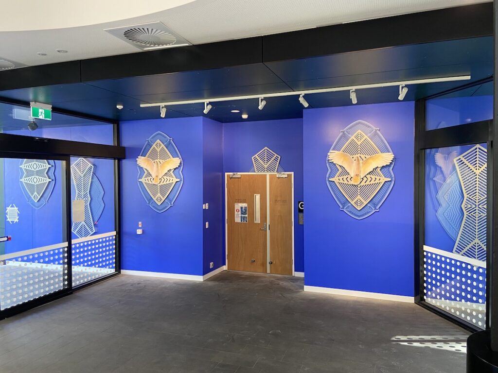 Bright blue office walls featuring geometric lines and cockatoo imagery on either side of a wooden door.
