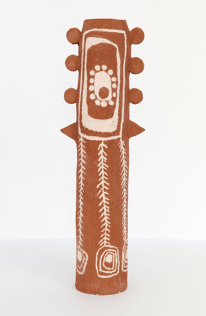 Abstract sculpture in red ochre and white colouring with abstract protrusions and carved patterning