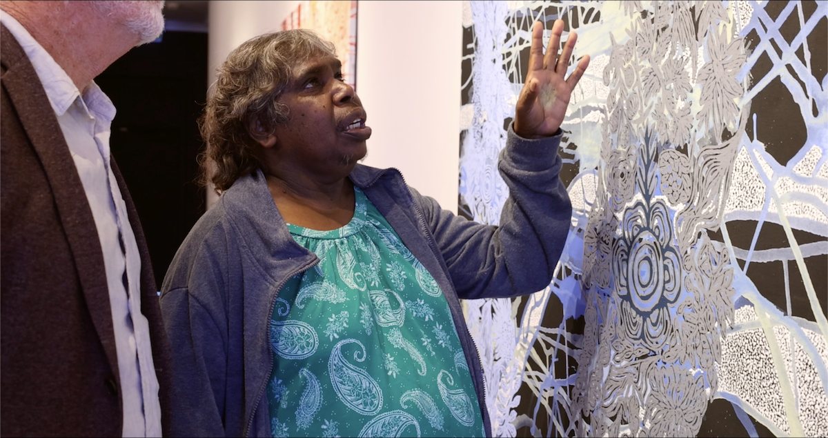 The artist gesturing towards her work as she describes its meaning to the figure on the left