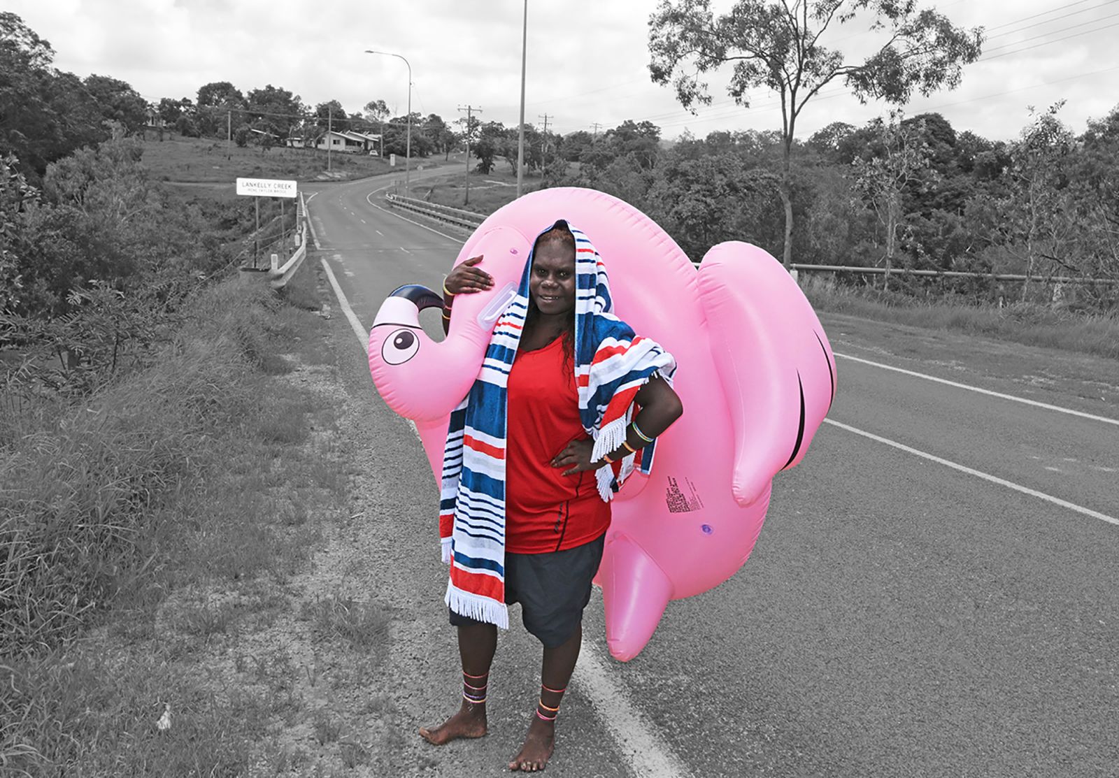 Young person standing roadside in beach attire with an inflatable flamingo beach toy.