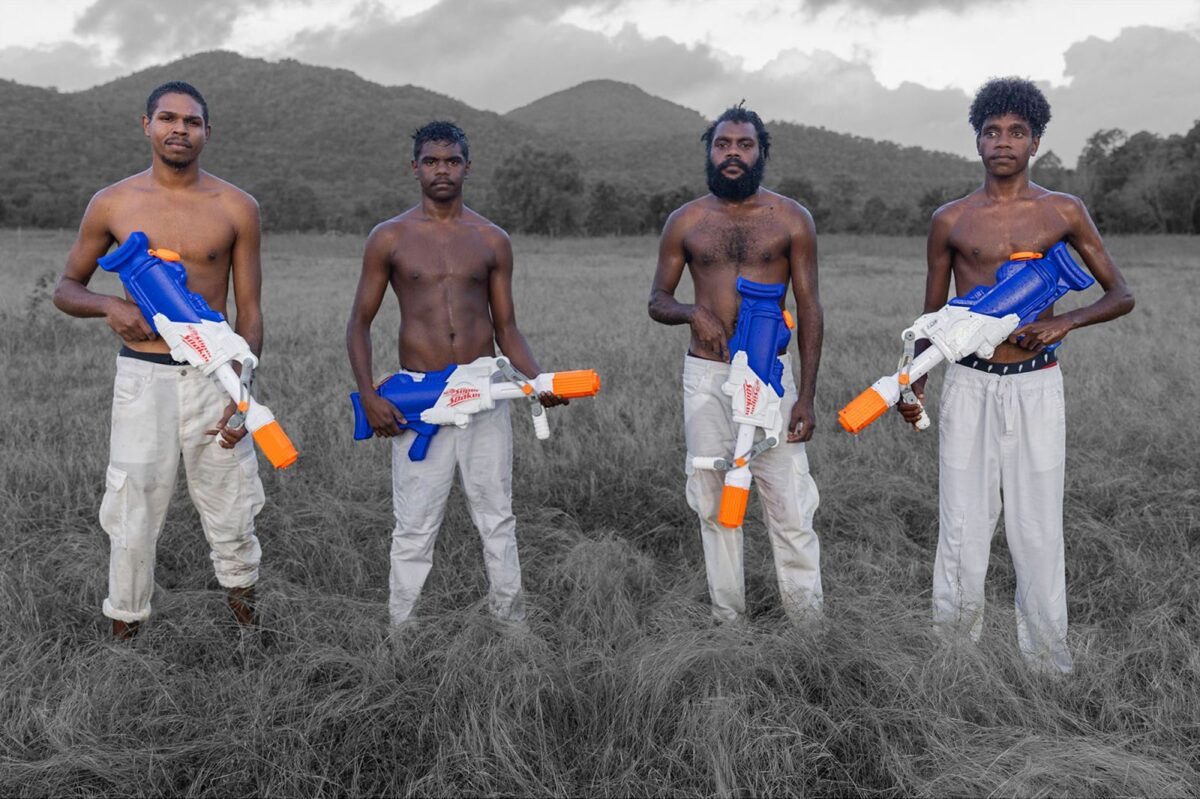 Four young people holding water guns in an open field.